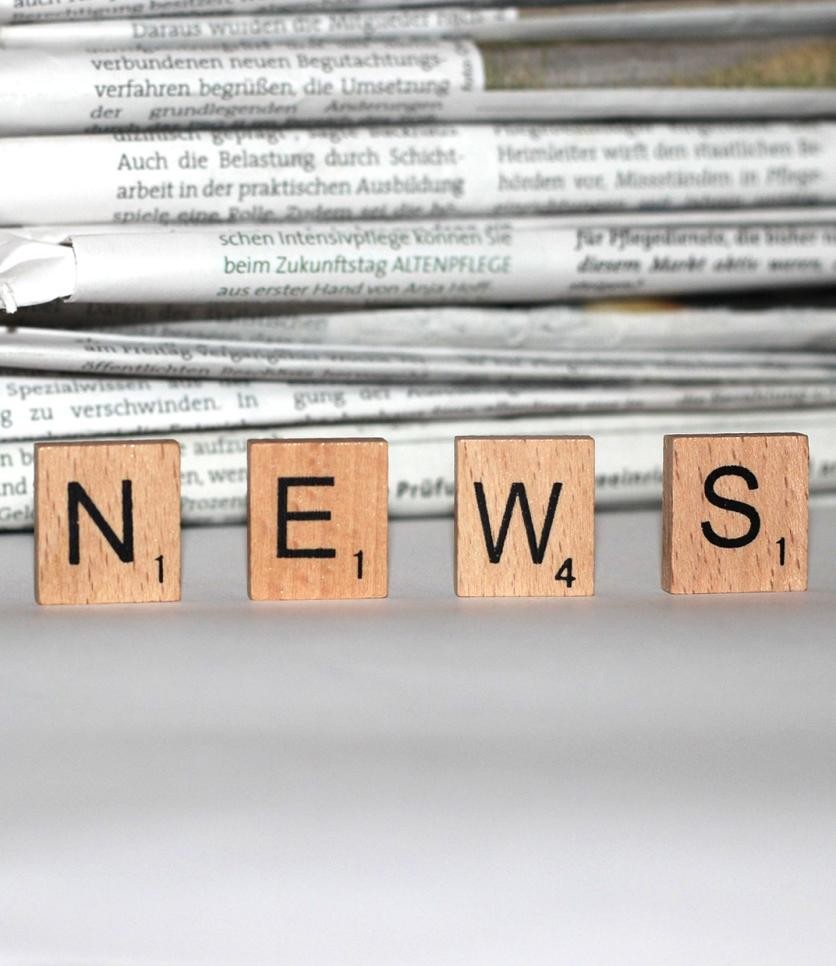 Newspapers lie on a table, wooden letters news stand in front of it