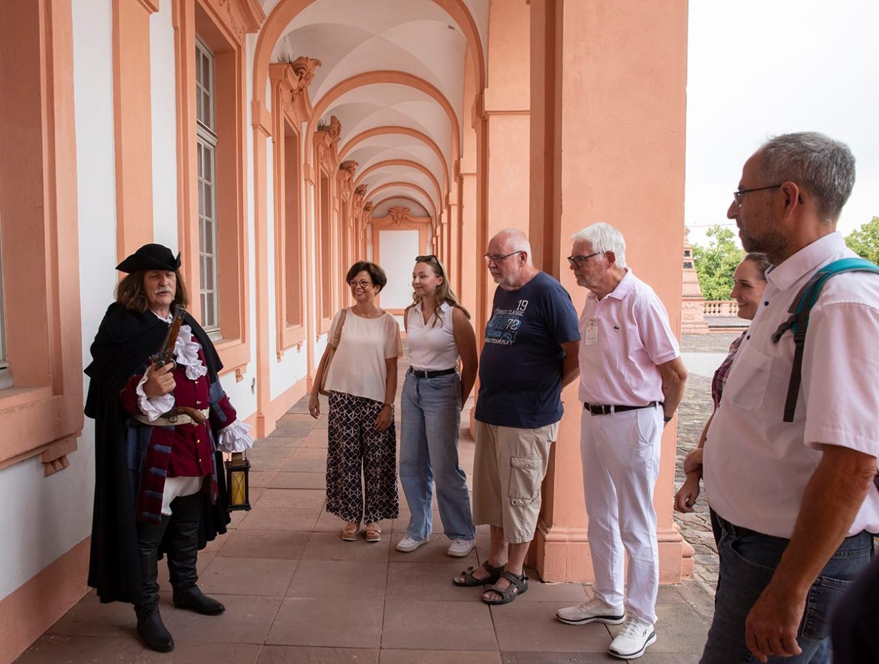 Bei der Nachtwächterführung geht es für die Teilnehmenden in der Dämmerung durch den historischen Stadtkern. Foto: Ulrike Klumpp Nachtwächter im Ehrenhof Schloss Rastatt mit Teilnehmer der Führung